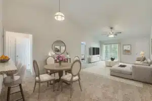 Open living and dining area with light walls, carpeted floor, round dining table, beige sectional sofa, TV, and large window with curtains.