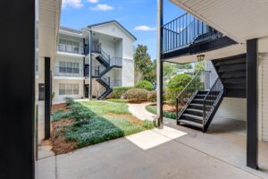 A courtyard view of a white, three-story apartment building with outdoor staircases and landscaped greenery.